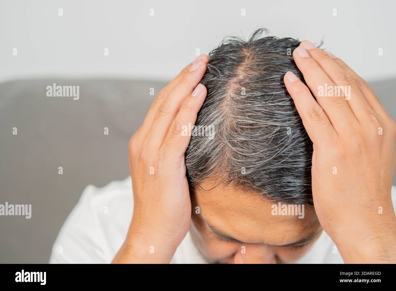 Nahaufnahme des Kopfes des Mannes mit grauem Haar an den Wurzeln, am Scheitel und an der Kopfhaut ist sichtbar, was auf das Altern hindeutet. Naturgraues Haarkonzept. Stockfoto