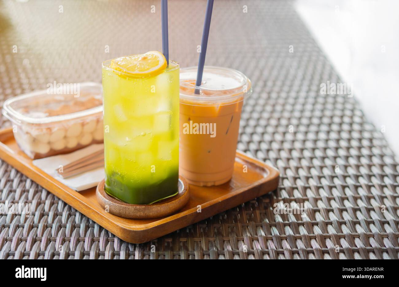 Ein köstliches süßes Essen mit Matcha Green Tea, frischer Zitrone, Eiskaffee und etwas Kuchen, serviert auf einem hölzernen Schneidebrett. Stockfoto
