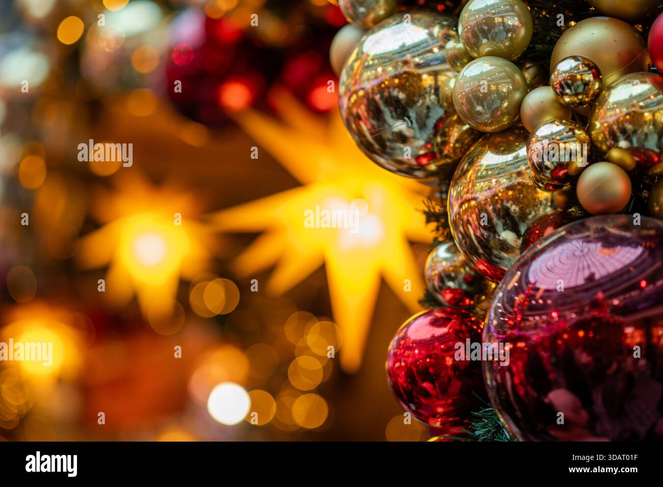 Goldene und rote Weihnachtskugeln mit einem leuchtenden Weihnachtsstern im weichen Bokeh-Hintergrund schaffen eine warme festliche Stimmung für saisonale Themen und Stockfoto