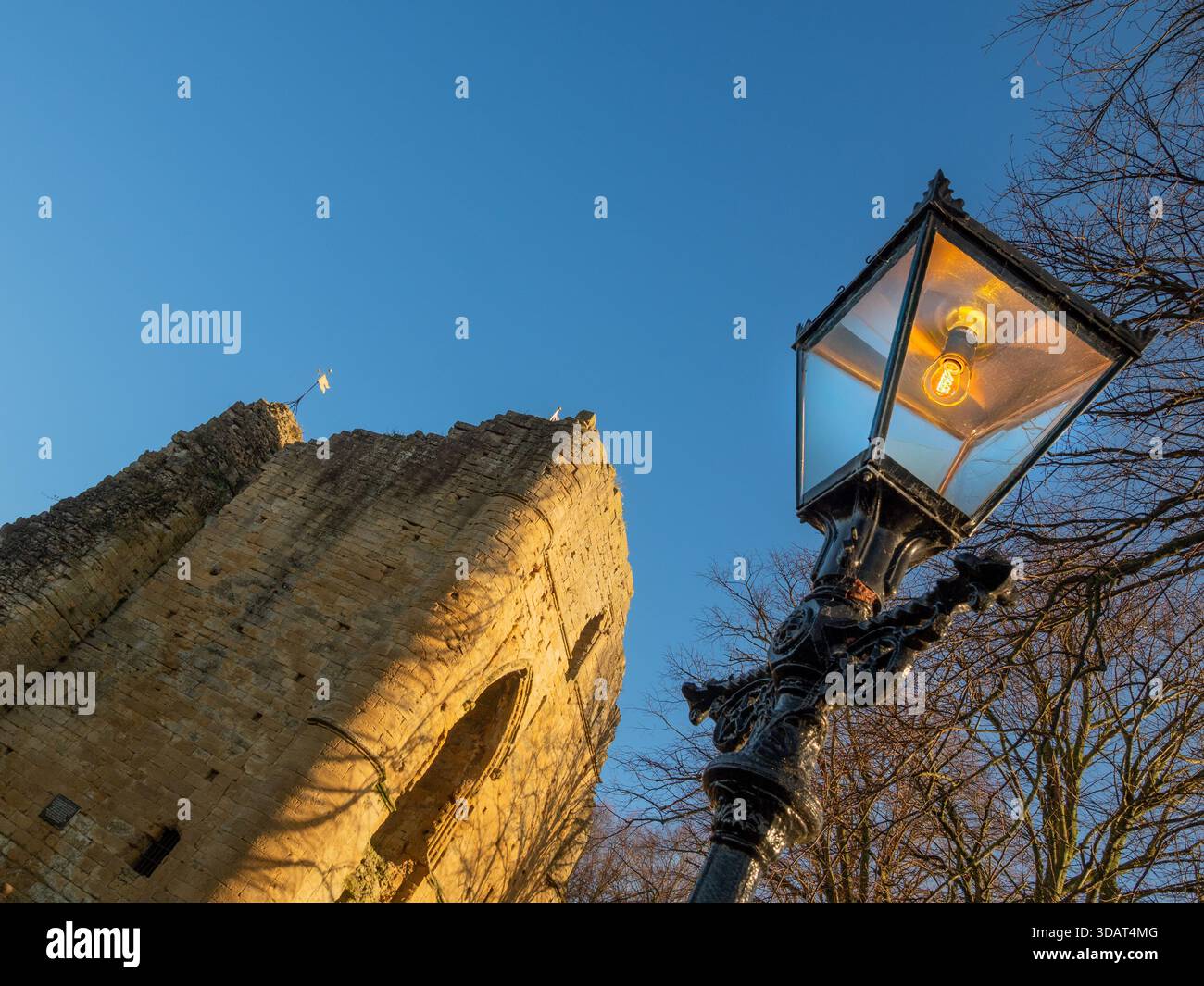 Ein alter schwarzer Gaslampen-Pfosten, der einen Blick auf die mittelalterlichen Ruinen von Knaresborough Castle vor einem blauen Himmel bietet. Stockfoto