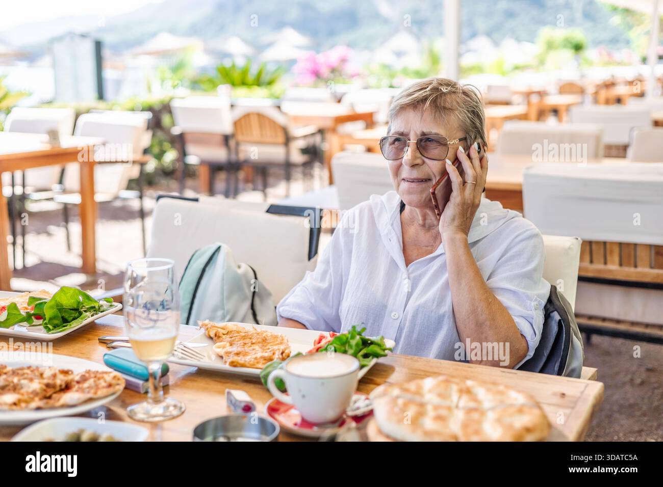 Eine ältere Frau mit Telefon sitzt im türkischen Restaurant am Strand Stockfoto