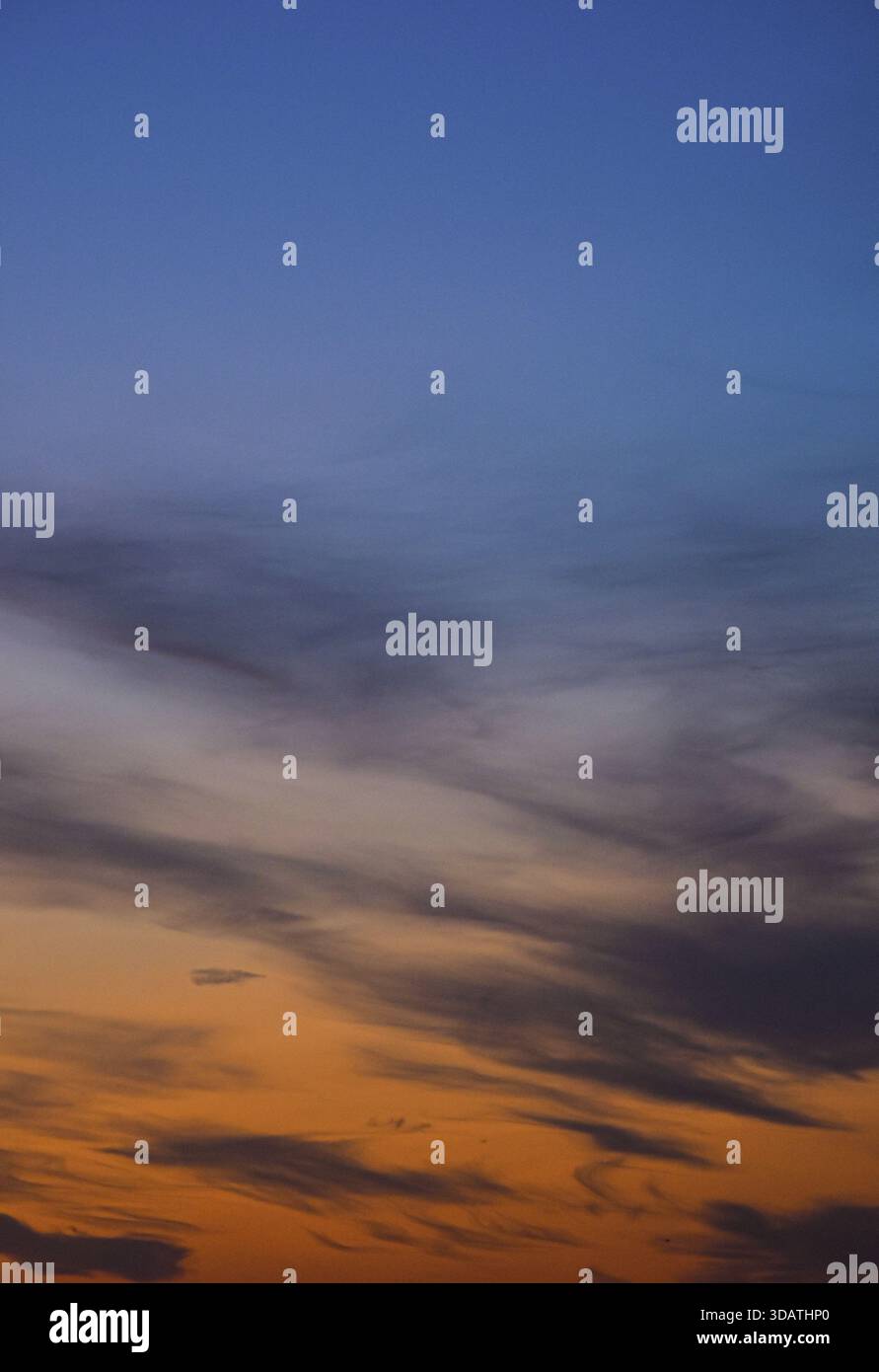 Ein dramatischer Nachmittagshimmel, der mit warmen Sonnenuntergangsfarben leuchtet, weiche Wolken, die von schwindendem Licht beleuchtet werden, schaffen einen beruhigenden und magischen natürlichen Moment. Stockfoto