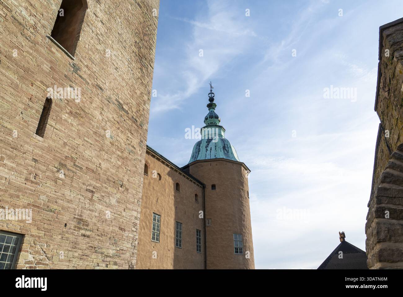 Blick auf die alten Ziegelmauern und Sandsteinmauern von Kalmar Castle, die sich zu einem Kupferturm erheben, vor dem Hintergrund der schimmernden Wolken und des blauen Himmels, Kalmar, Kalm Stockfoto