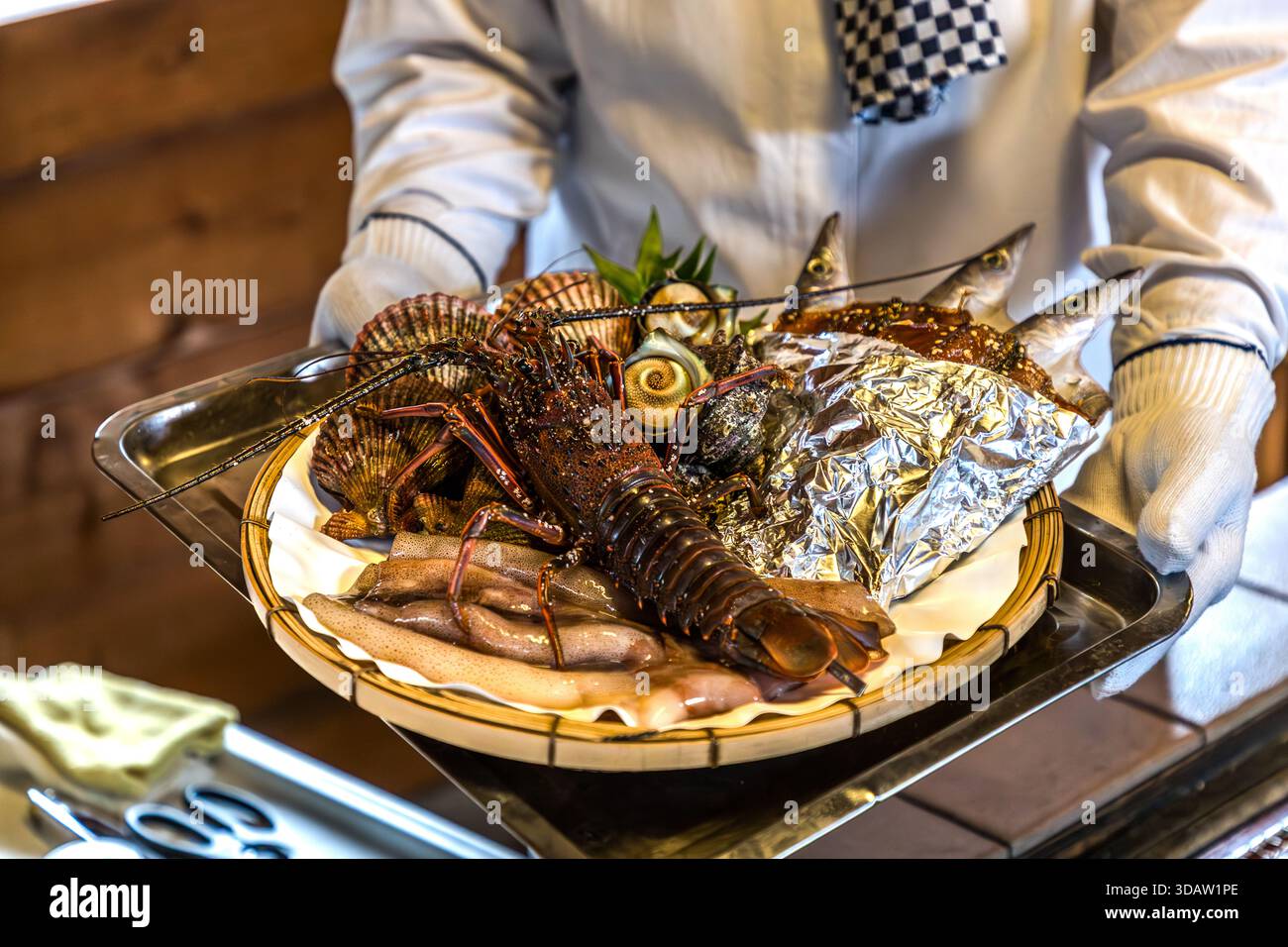 Ise-Hummer, Tintenfisch, Jakobsmuscheln, Turbanmuschel und japanischer Makrelen machen das Deluxe-Platte aus, das von einer Ama-Taucherin bei der Ama Hut Experience und Lunch im Satoumian Ama Hut, Shima, Präfektur Mie, Japan, präsentiert wird. Während der Ama Hut Experience grillen Ama-Taucherinnen frisch gefangene Meeresfrüchte für die Gäste in einer Nachbildung einer Ama-Hütte und verbinden dabei Kultur, Geschichte und Küche. Stockfoto