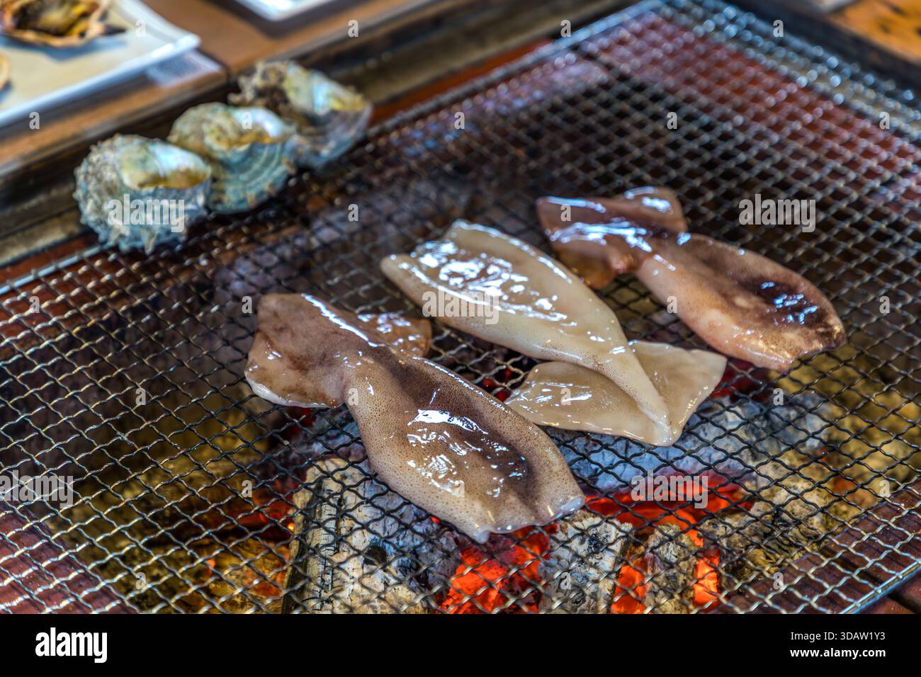 Tintenfisch brutzelt auf dem offenen Holzkohlegrill der Ama Hut Experience in Shima, Präfektur Mie, Japan. Traditionell bereiteten die Ama-Taucher auch ihr eigenes Mittagessen aus frisch gefangenen Meeresfrüchten zu. Stockfoto
