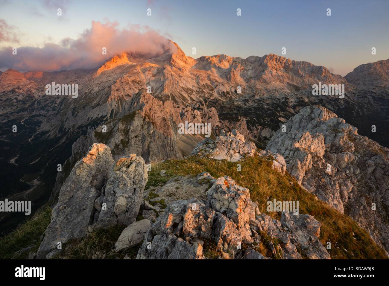 Aus der Vogelperspektive auf dramatische Gipfel und zerklüftetes Gelände im warmen Glanz des Sonnenaufgangs, mit Wolken, die sich an den Gipfel Klammern, Triglavski narodni Park, Gore Stockfoto