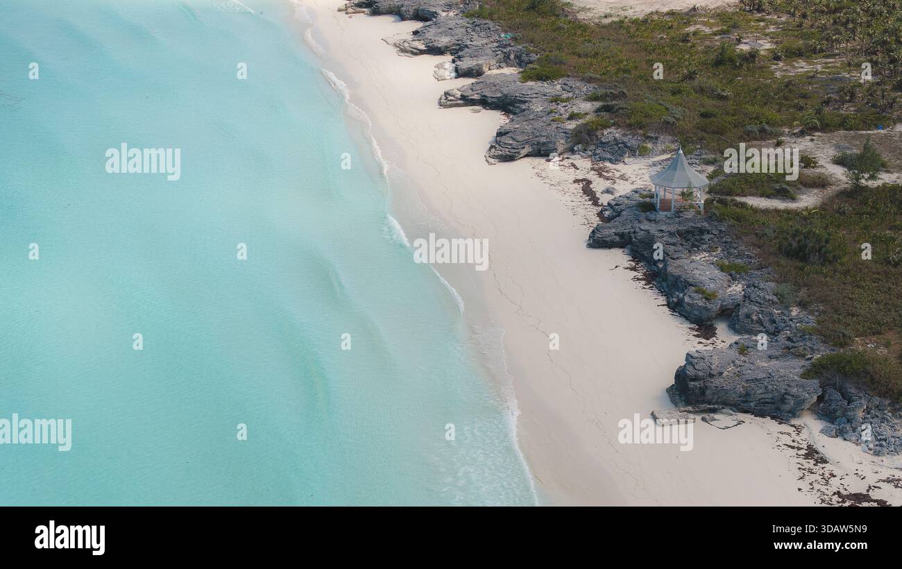 Aus der Vogelperspektive auf das türkisfarbene Meer trifft auf den weichen Sandstrand in der Nähe von felsigen Ausbissen und karger Vegetation, Great Harbour Cay, Berry Islands und Bahama Stockfoto