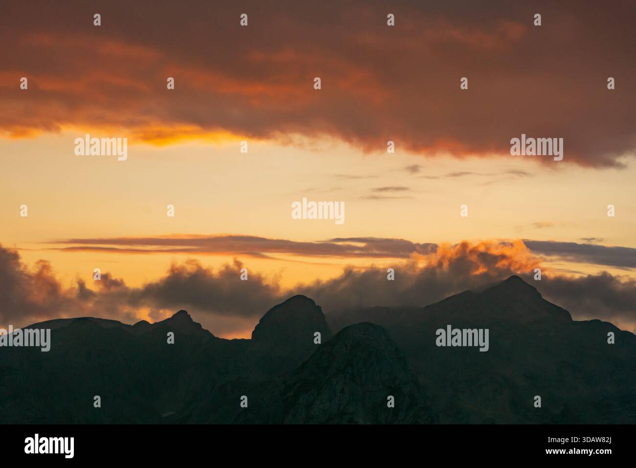 Aus der Vogelperspektive auf die Berge von Tosc vor einem feurigen Himmel, wo Orange- und Goldtöne die Wolken über dem Triglavski narodni Park, Gorenjska, prägen Stockfoto