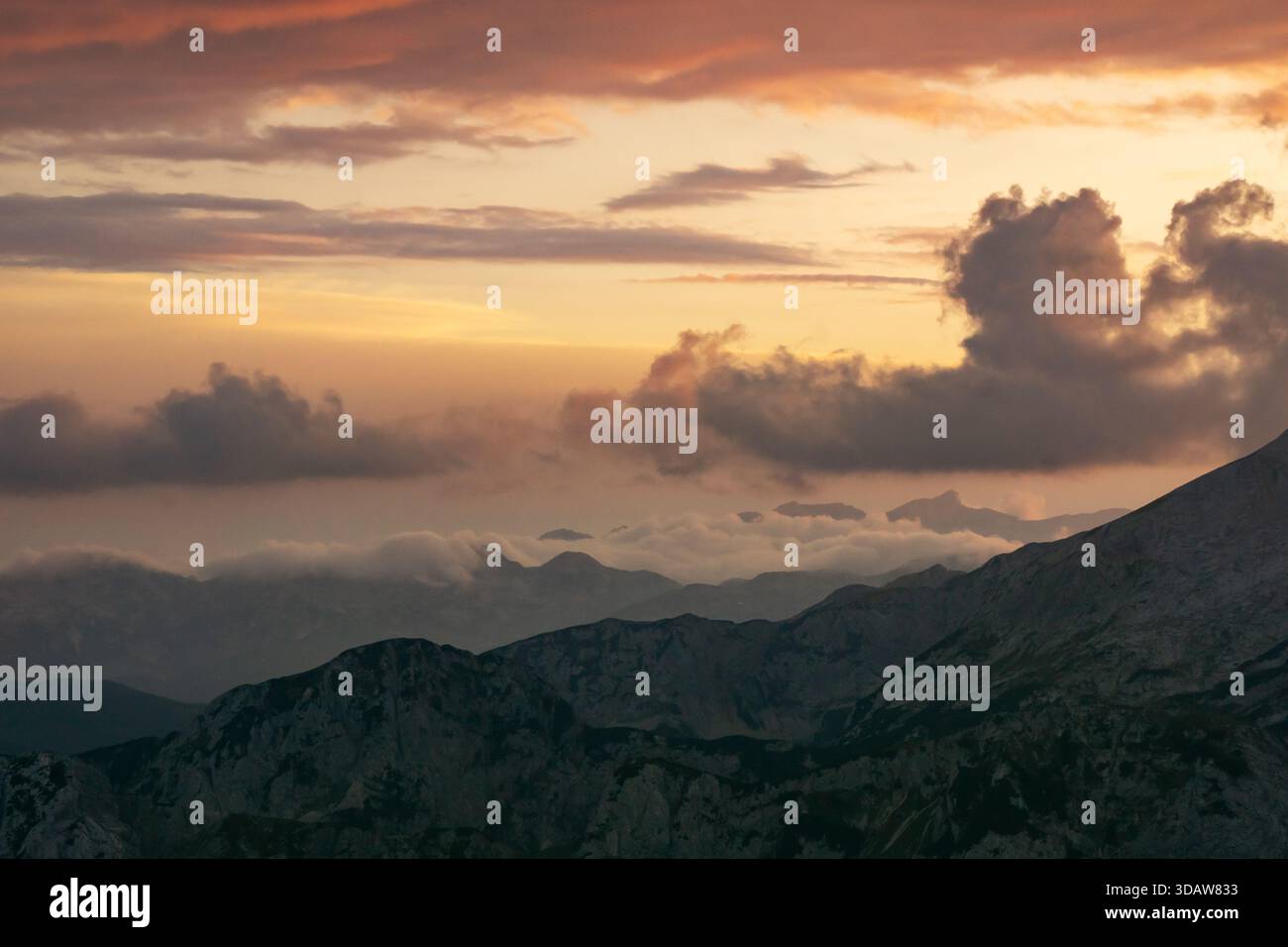 Aus der Vogelperspektive auf die zerklüfteten Gipfel von Tosc unter einem dramatischen Himmel, der mit feurigen Orange- und Violetttönen bemalt ist, Triglavski narodni Park, Gorenjska, Sloveni Stockfoto