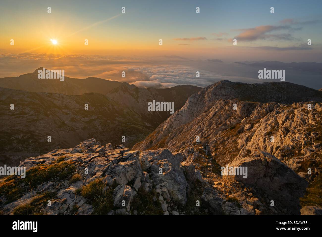 Aus der Vogelperspektive auf das strahlende Licht der Sonne, das die zerklüfteten Gipfel von Tosc küsst, mit Wolken in Tälern, Triglavski narodni Park, Gorenjska, Slowenien. Stockfoto