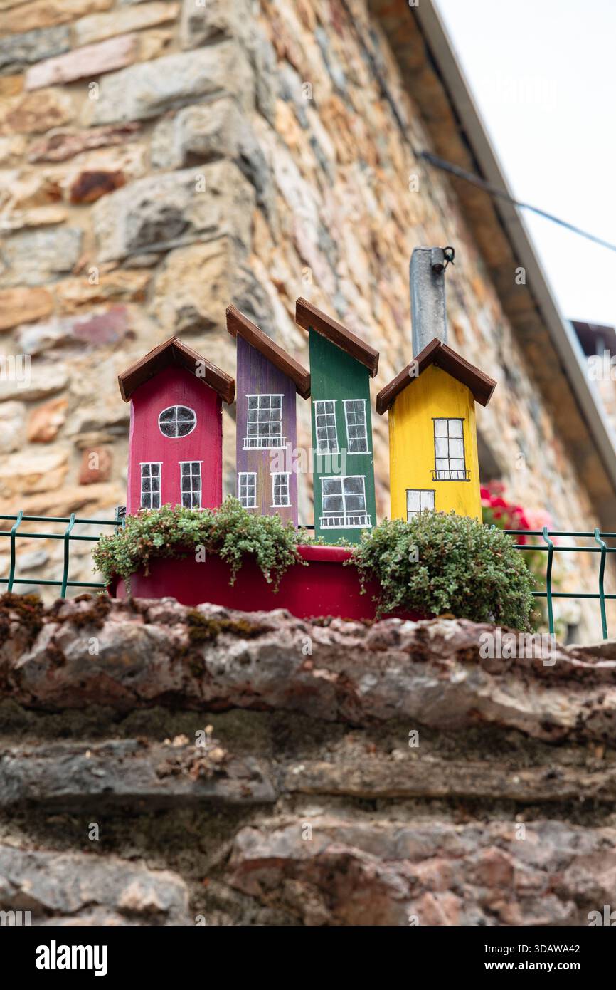 Eine bezaubernde Sammlung von bunten hölzernen Miniaturhäusern befindet sich auf einer Steinmauer mit grünen Pflanzen vor der rustikalen Kulisse des Stockfoto