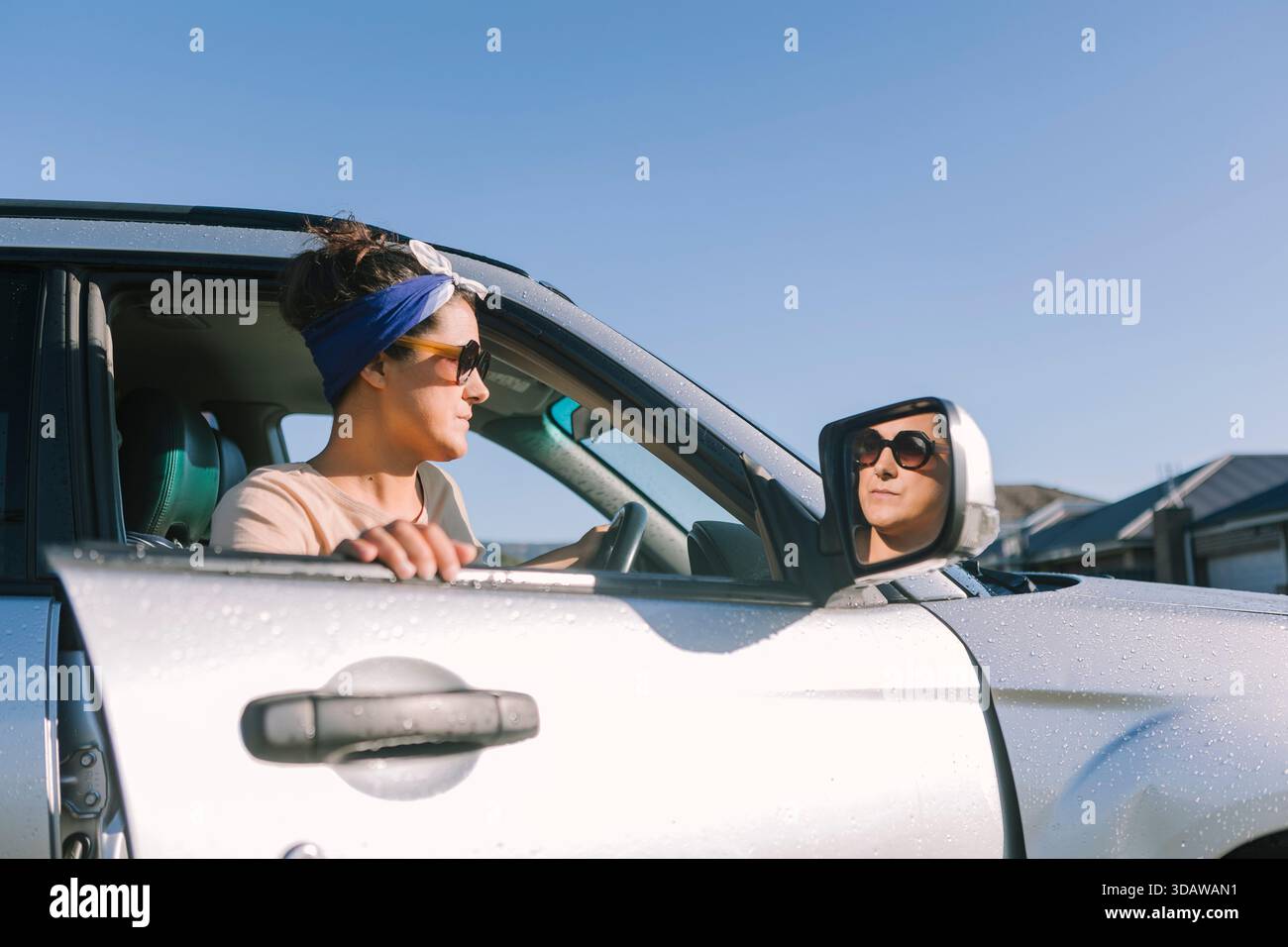 Eine Frau mit Sonnenbrille und Stirnband in ihrem silbernen Auto, die an einem sonnigen Tag in Australien kaputt ist. Sie schaut sich um und sucht möglicherweise nach Stockfoto
