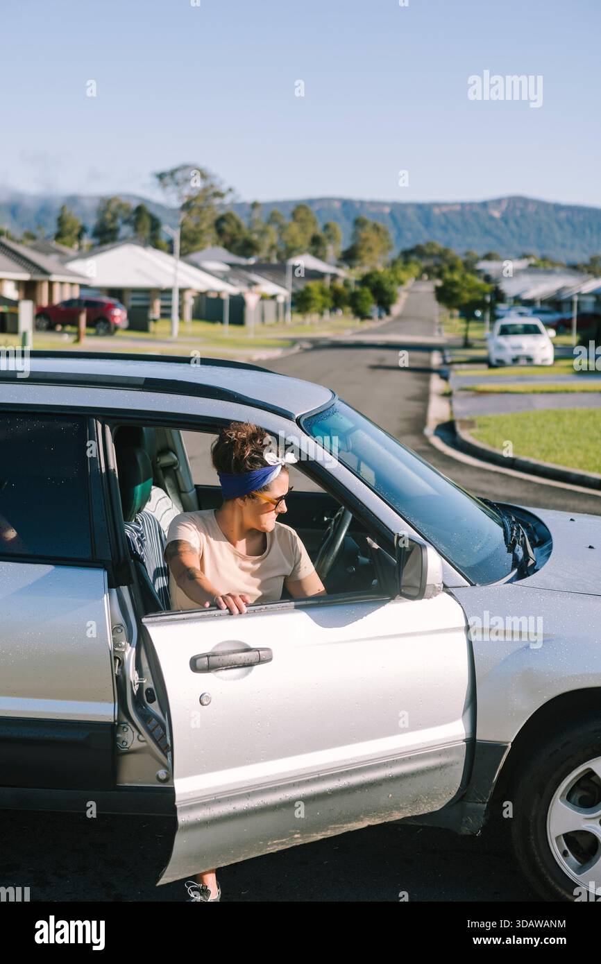 Eine Frau sieht besorgt neben ihrem kaputten Auto in einer Vorstadtstraße in Australien aus. Sie lehnt sich aus ihrem Fahrzeug und bewertet die Situation auf einem sunn Stockfoto