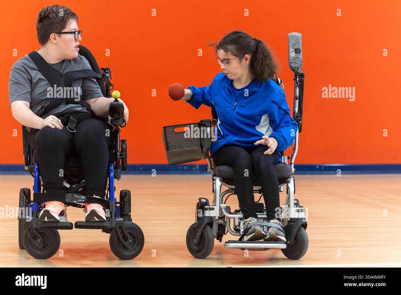 Zwei Boccia-Spieler mit Zerebralparese-Praxis im Rollstuhl mit Schwerpunkt Wurftechnik. Sie nehmen an einem Training auf einem Hallenplatz Teil Stockfoto