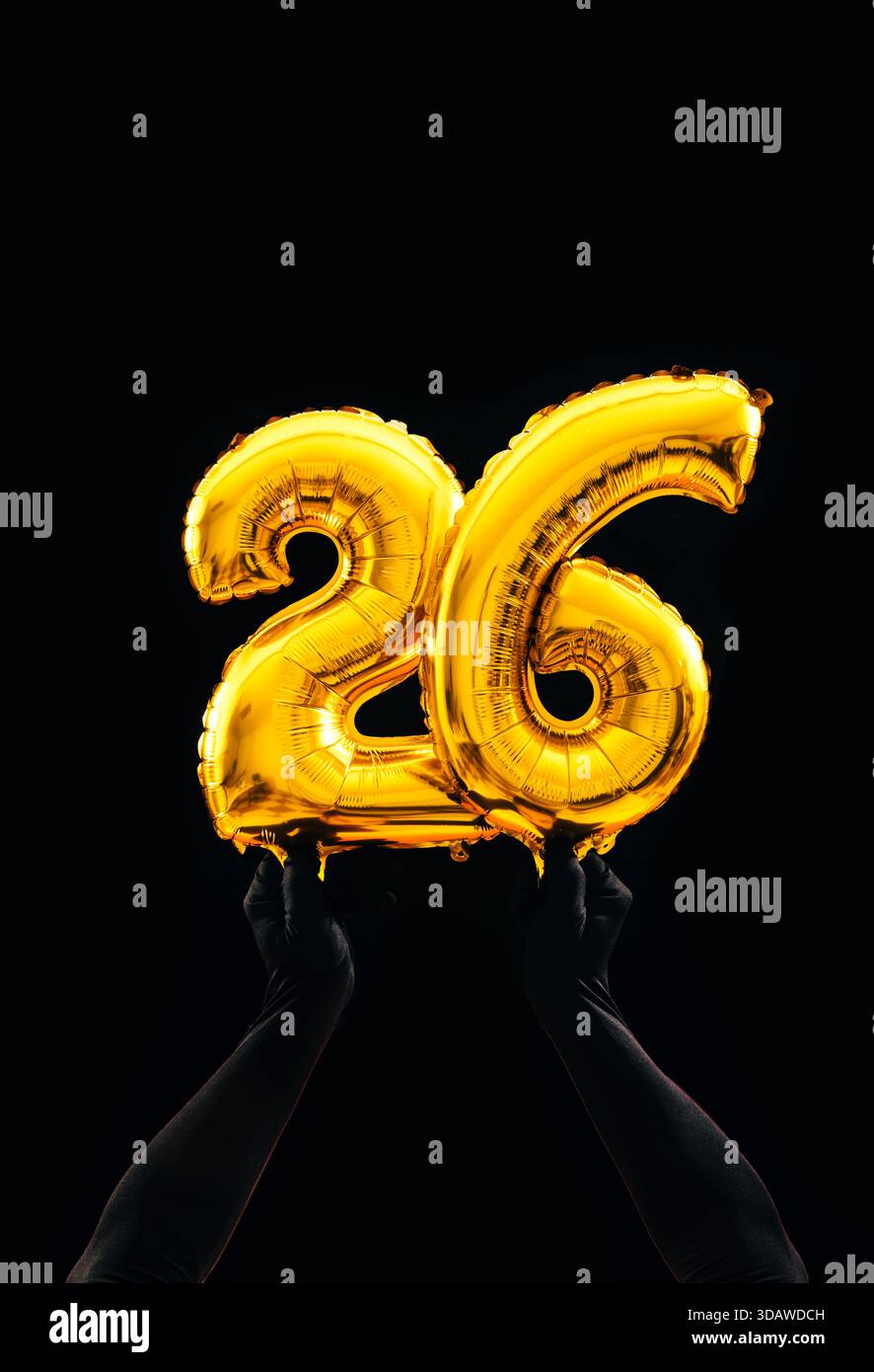 Die Hände halten die goldenen Zahlenballons 26 vor dunklem Hintergrund und symbolisieren eine festliche Feier, perfekt für Geburtstage, Jahrestage oder N Stockfoto