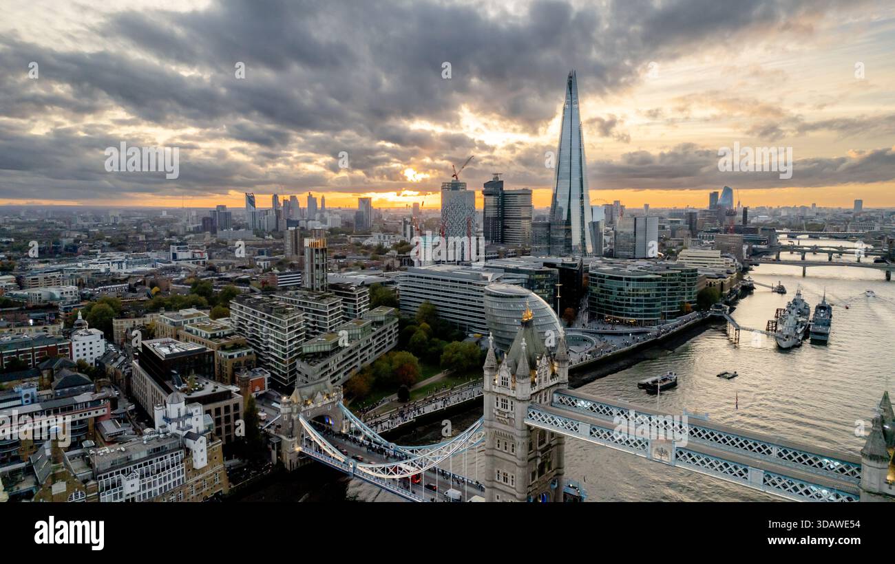 Fesselnde Luftaufnahme von Londons Tower Bridge, mit dem berühmten Shard im Hintergrund, während eines atemberaubenden Sonnenuntergangs. Die Themse schlängelt sich durch den Fluss Stockfoto