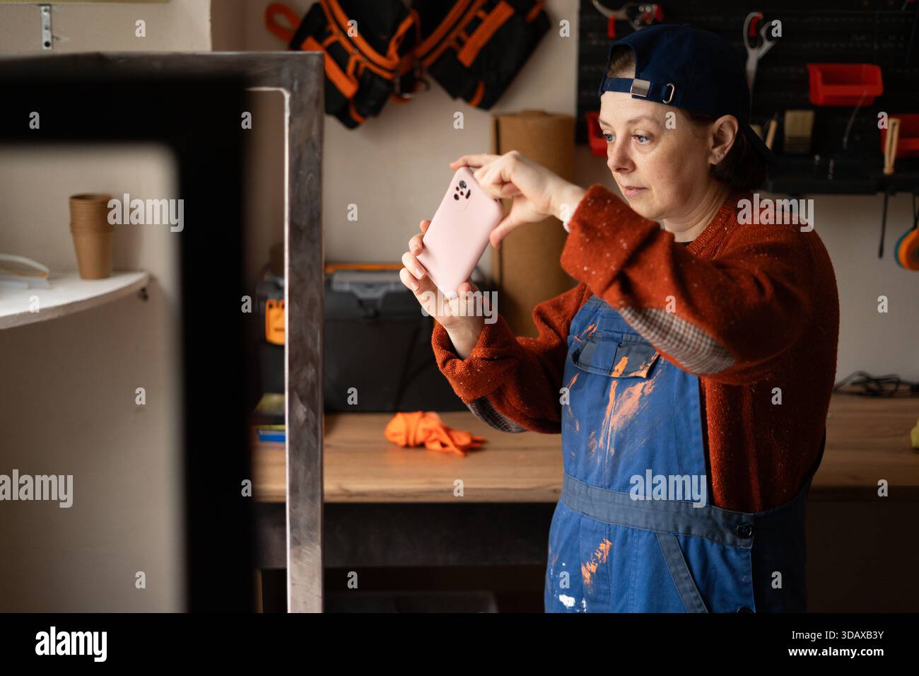 Junge professionelle Mechanikerin oder Handwerkerin Frau in blauem Overall fotografieren auf Handy beheben Probleme in Reparatur Renovierungswerkstatt beheben. Stockfoto