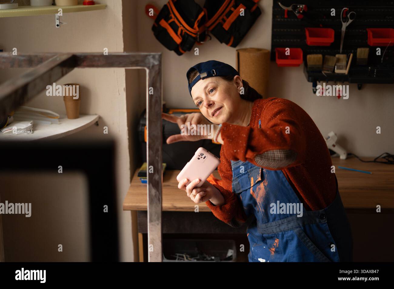 Junge professionelle Mechanikerin oder Handwerkerin Frau in blauem Overall fotografieren auf Handy beheben Probleme in Reparatur Renovierungswerkstatt beheben. Stockfoto