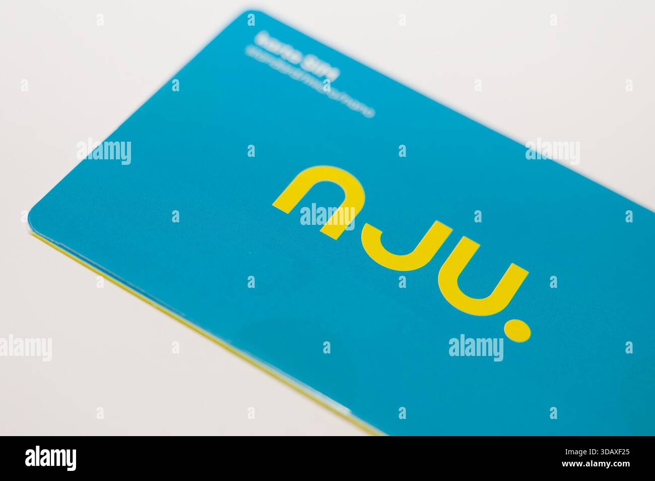 Nahaufnahme des Nju SIM-Kartenpakets in Türkis mit gelbem Logo, fotografiert auf einer weißen Oberfläche. Stockfoto