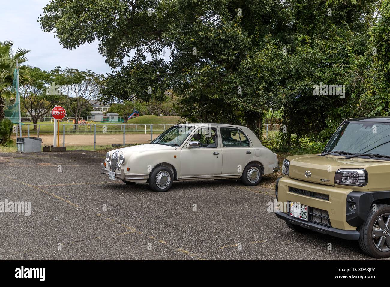 Ein älteres Auto ist neben einem modernen SUV auf einem Asphaltparkplatz in Taiji, Präfektur Wakayama, Japan, geparkt. Stockfoto