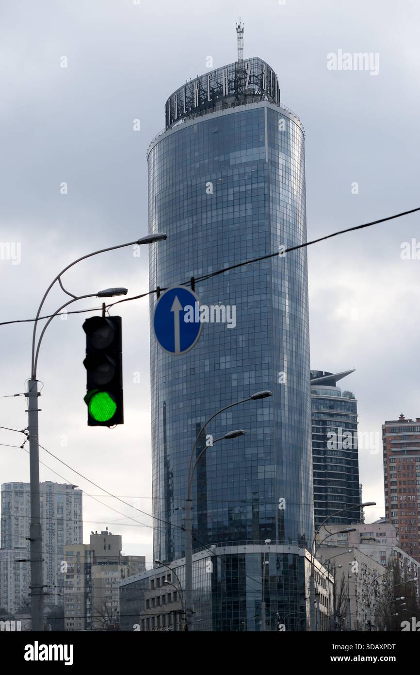 Ein eleganter Wolkenkratzer überragt die Straßen der Stadt unter einem leuchtend grünen Signal. Kiew, Ukraine. Dezember 2025. Stockfoto
