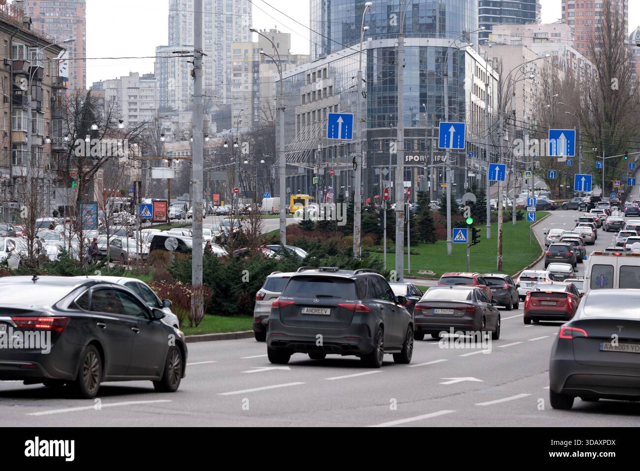 Die Autos fahren entlang einer belebten Straße, die mit Richtungsschildern und Gebäuden gesäumt ist. Kiew, Ukraine. Dezember 2025. Stockfoto