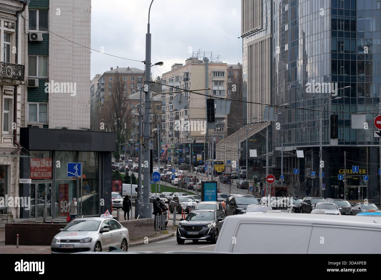 Autos und Menschen strömen an einem bewölkten Tag durch ein lebhaftes Stadtzentrum. Kiew, Ukraine. Dezember 2025. Stockfoto