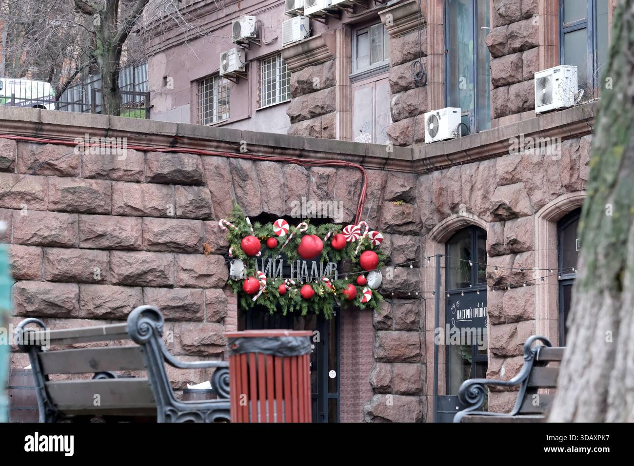 Leuchtend rote Ornamente und Bänder zieren eine bezaubernde Steintür und laden alle ein. Kiew, Ukraine. Dezember 2025. Stockfoto