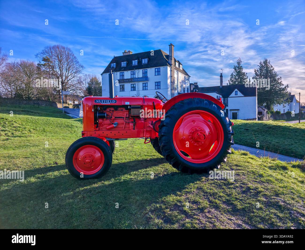 Classic Red Vintage Traktor mit Cotswolds Manor House im Hintergrund Stockfoto
