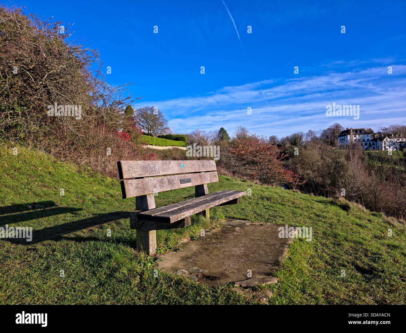 Holzbank umgeben von Büschen mit Blick auf das Dorf in der Landschaft von Cotswolds Stockfoto