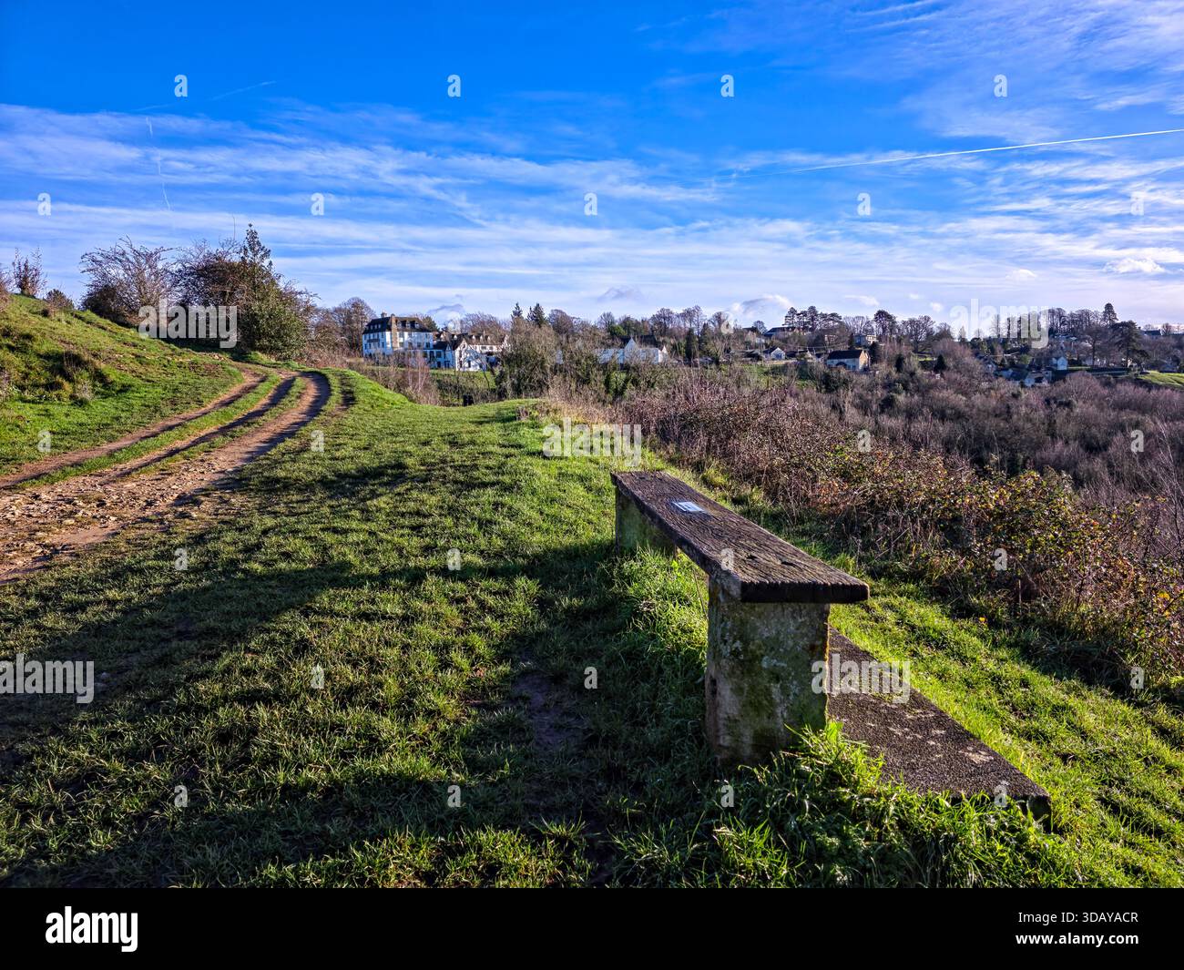 Holzbank auf einem Hügel mit Blick auf das malerische Dorf in der Landschaft von Cotswolds Stockfoto