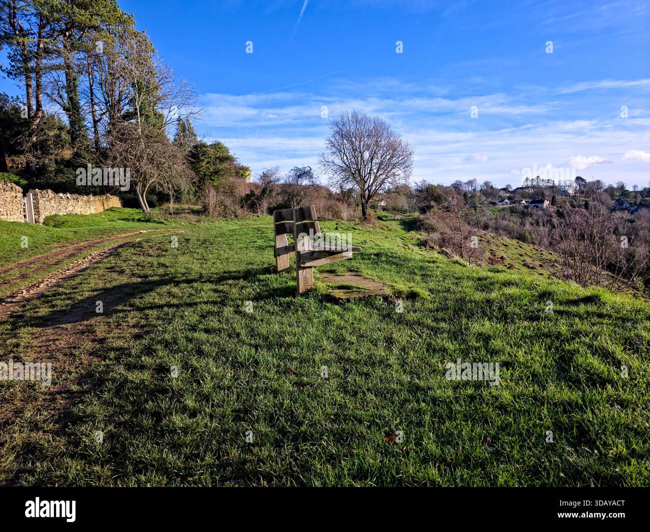 Holzbank am ländlichen Fußweg mit Blick auf das Tal in der Landschaft von Cotswolds Stockfoto