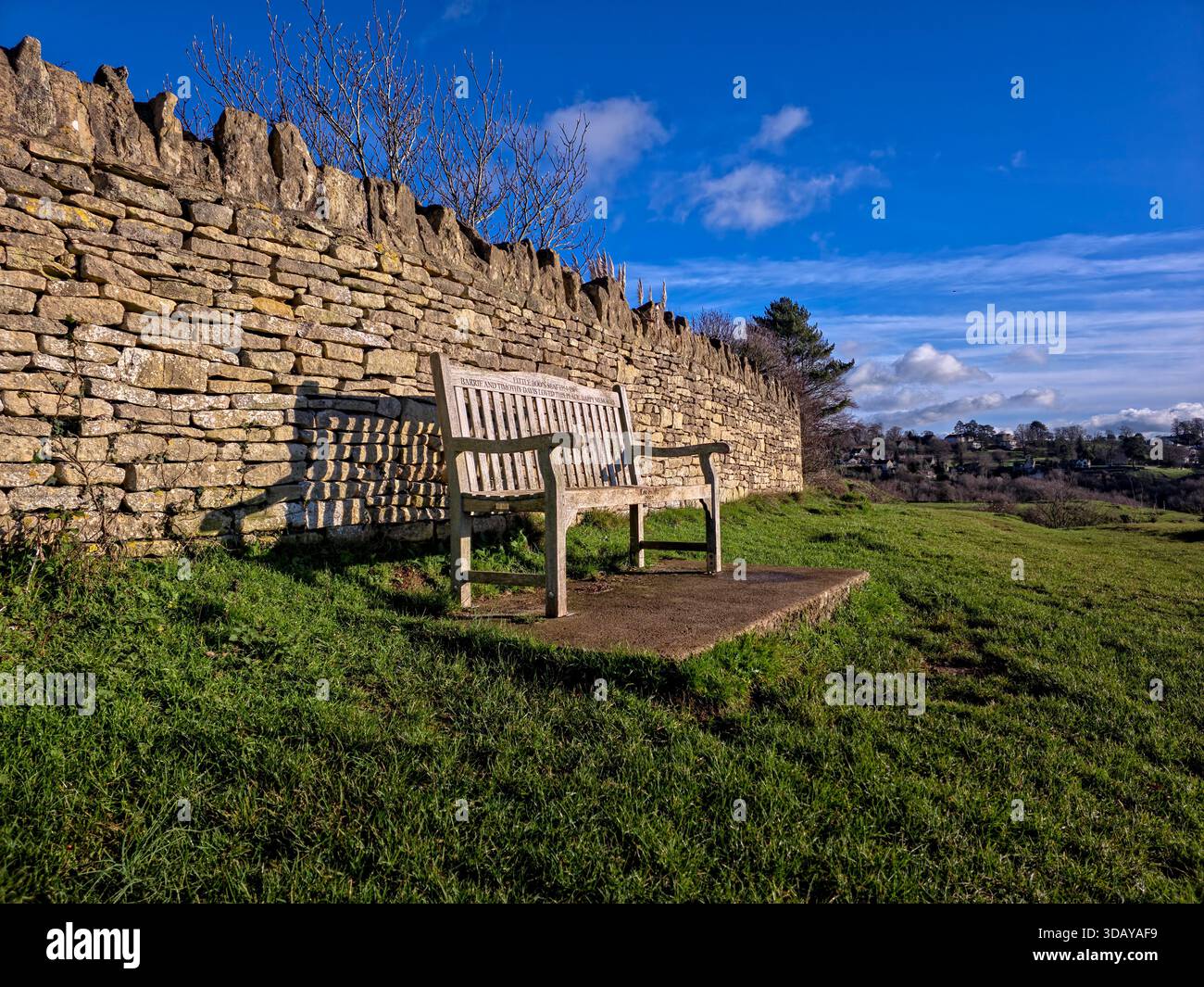 Holzbank an der traditionellen Trockenmauer in Cotswolds Landschaft Stockfoto