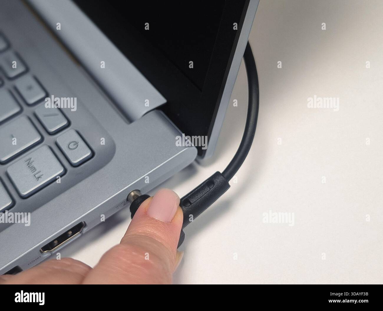 Nahaufnahme des Handsteckens des runden Ladekabels in den Netzanschluss des Laptops Stockfoto