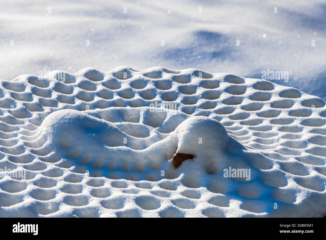 Helles Sonnenlicht strahlt auf einen Picknicktisch aus Metall, der mit komplizierten Schneemustern bedeckt ist und die Schönheit des Winters in Ludington, Michigan, zeigt. Stockfoto