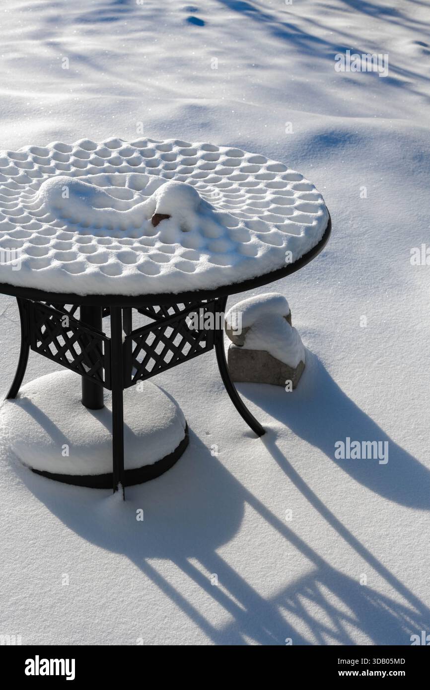 Ein mit Schnee bedeckter Picknicktisch aus Metall zeigt wunderschöne Muster unter strahlender Sonne und bringt eine ruhige Winterszene nach Ludington, Michigan. Stockfoto