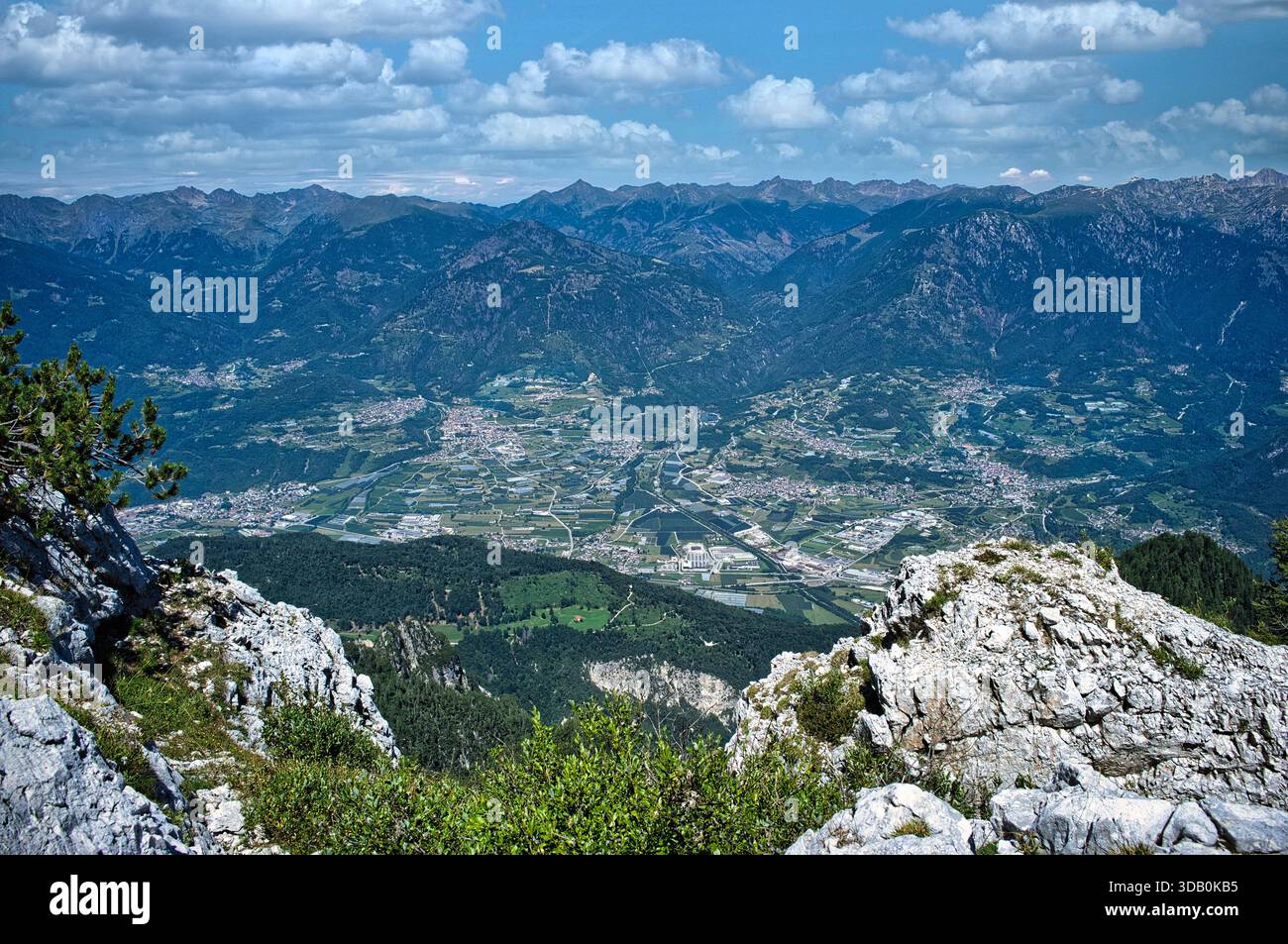 Hochauflösender Panoramablick von einem felsigen Berggipfel mit Blick auf ein weites Alpental mit kleinen Städten, bewirtschafteten Feldern, Wäldern, A Stockfoto