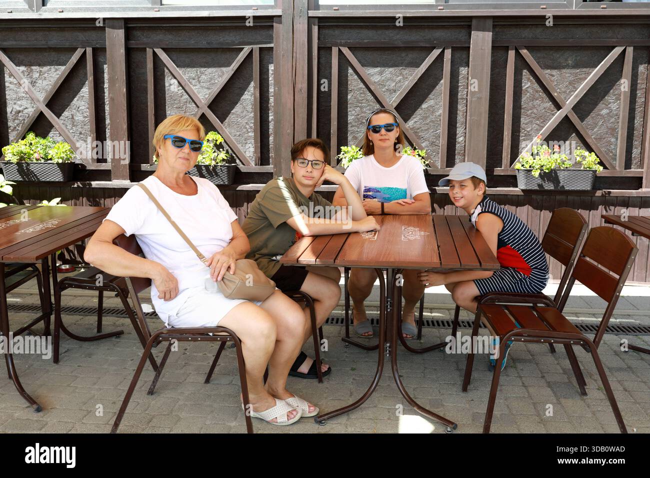 Frau, Mann, Junge und Kind sitzen am Tisch im Freien. Familie zusammen im Sommerurlaub. Generationsübergreifendes Treffen im Restaurant. Stockfoto