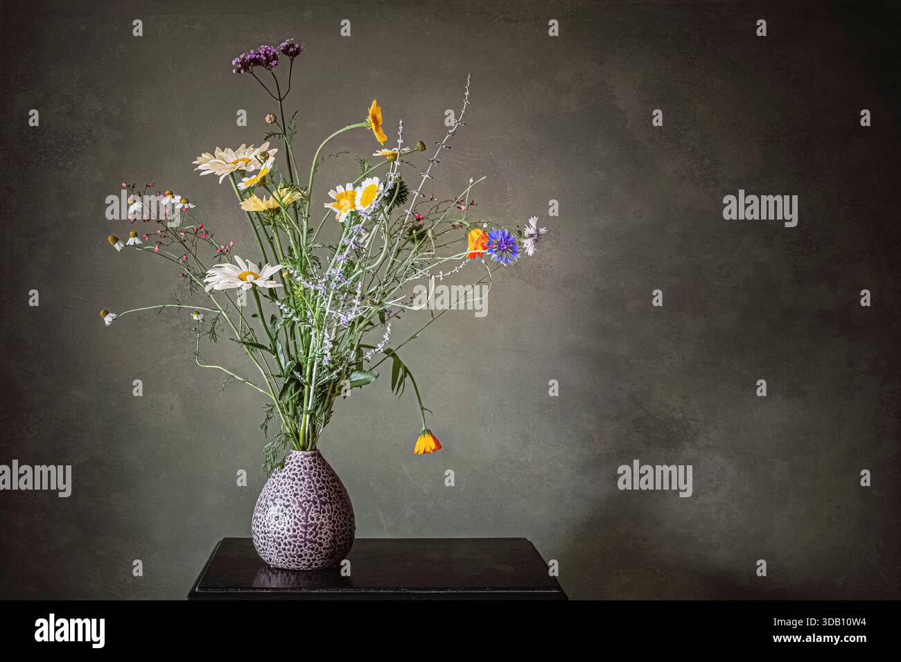 Blumenstrauß aus Wildblumen in einer kleinen Vase vor grauem Hintergrund. Stockfoto