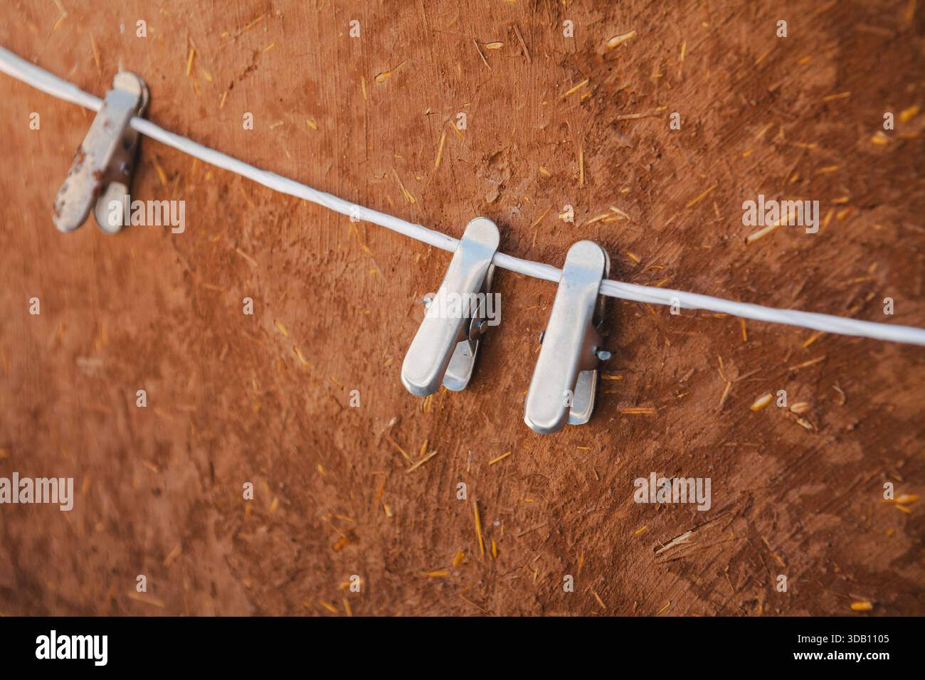Drei Metallkleideräume auf einem dünnen weißen Draht. Strukturierter brauner Hintergrund. In gleichmäßigen Abständen werfen sie weiche Schatten. Stockfoto