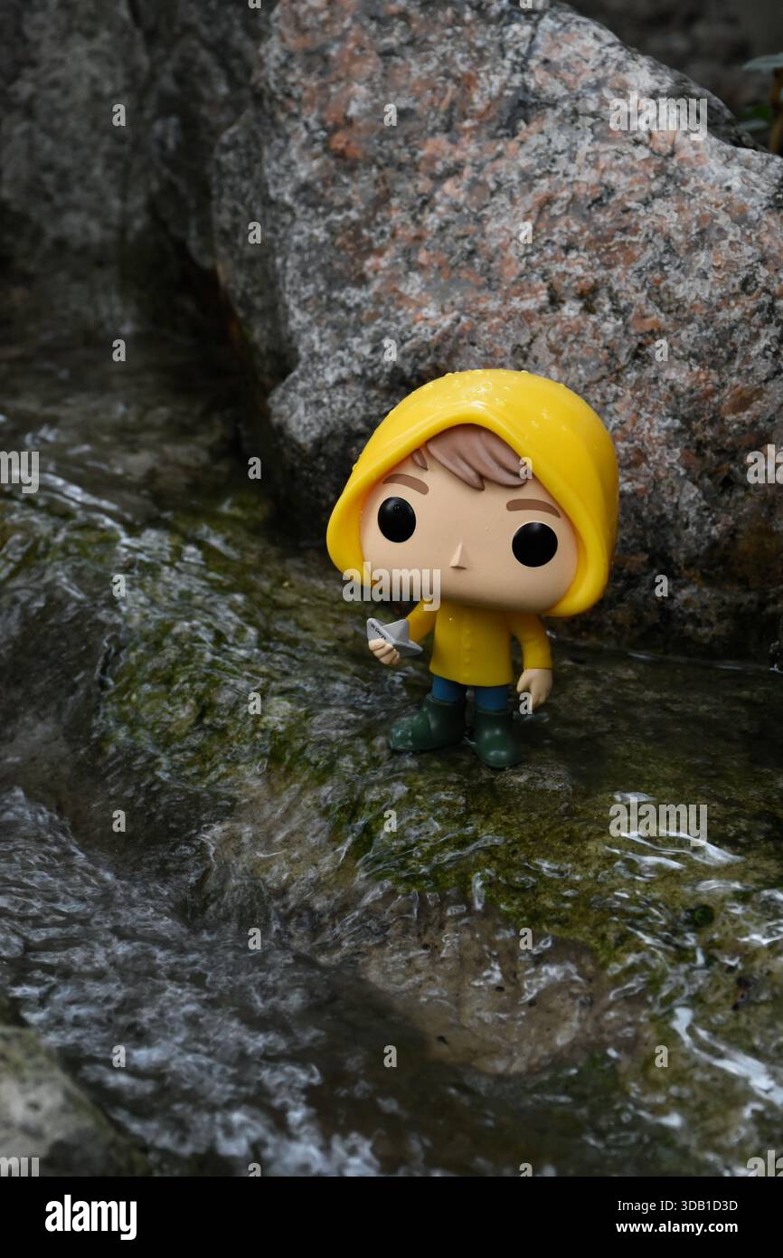 Funko Pop Actionfigur von Georgie Denbrough aus dem Horrorfilm IT. Junge mit Papierboot steht zwischen Felsen am Fluss. Stockfoto