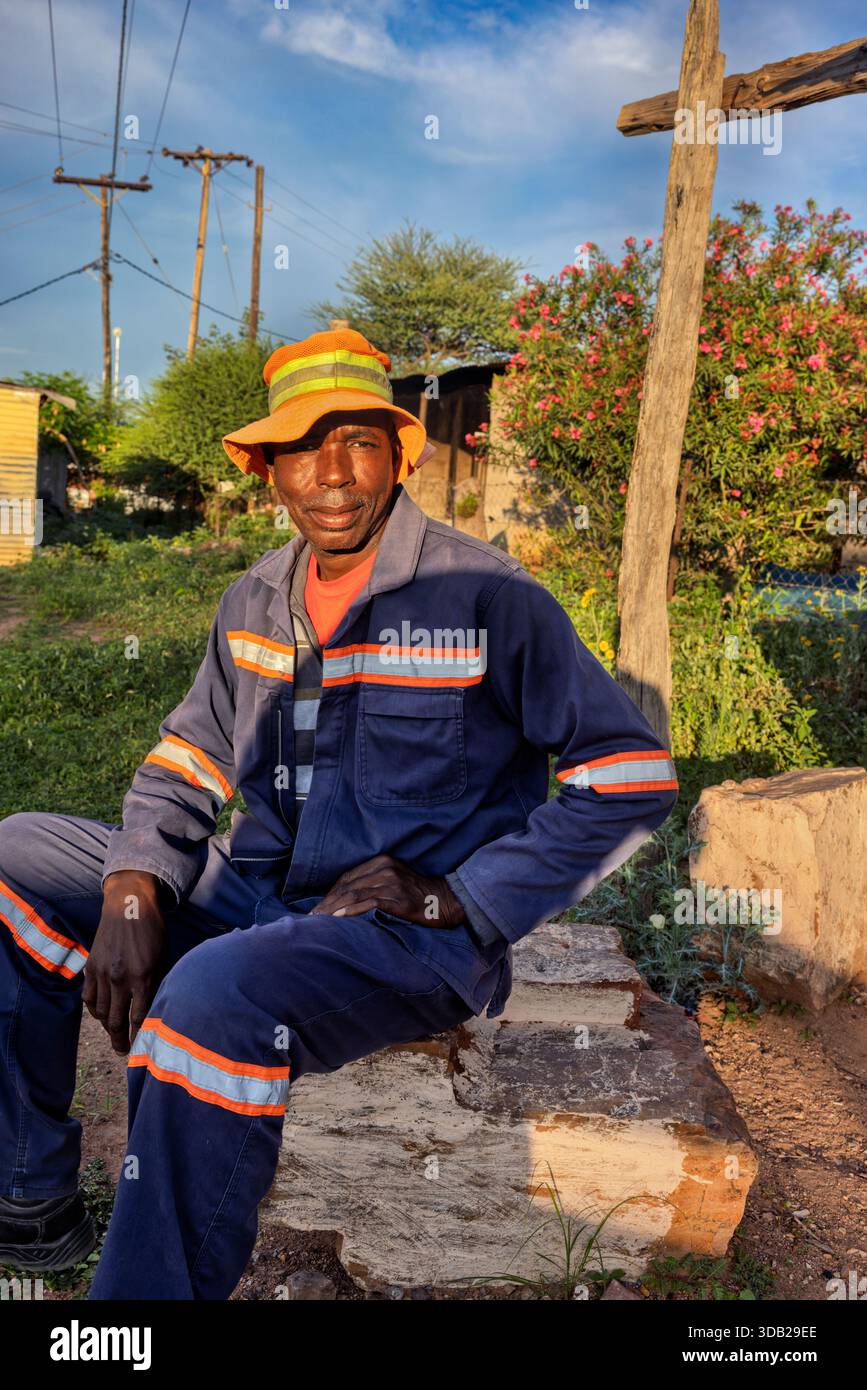 Einzelne afrikanische Männer sitzen draußen auf einer Steinbank bei Sonnenaufgang, Einstellung mit gewellten Metall- und Holzstützen, Johannesburg, Südafrika, blauer wo Stockfoto