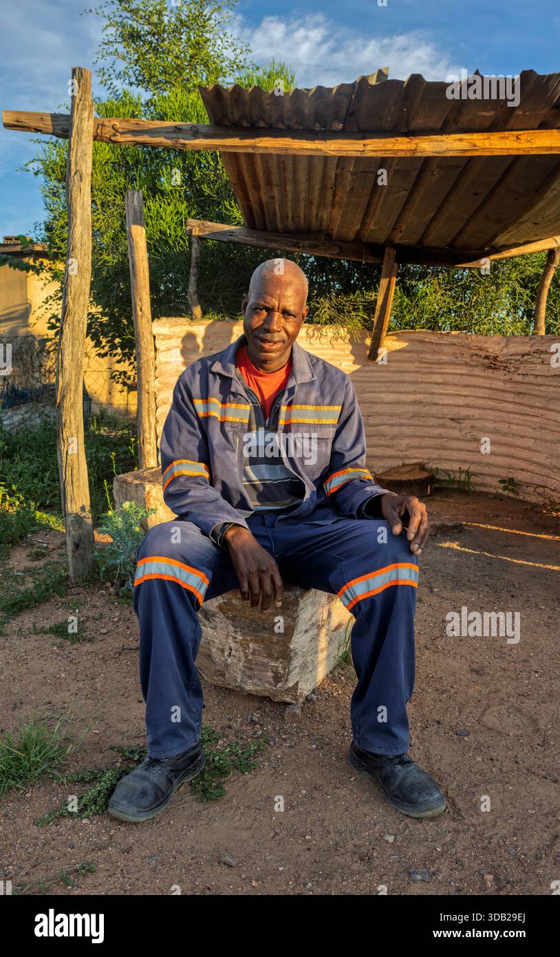 Einzelne afrikanische Männer sitzen draußen auf einer Steinbank bei Sonnenaufgang, Einstellung mit gewellten Metall- und Holzstützen, Johannesburg, Südafrika, blauer wo Stockfoto
