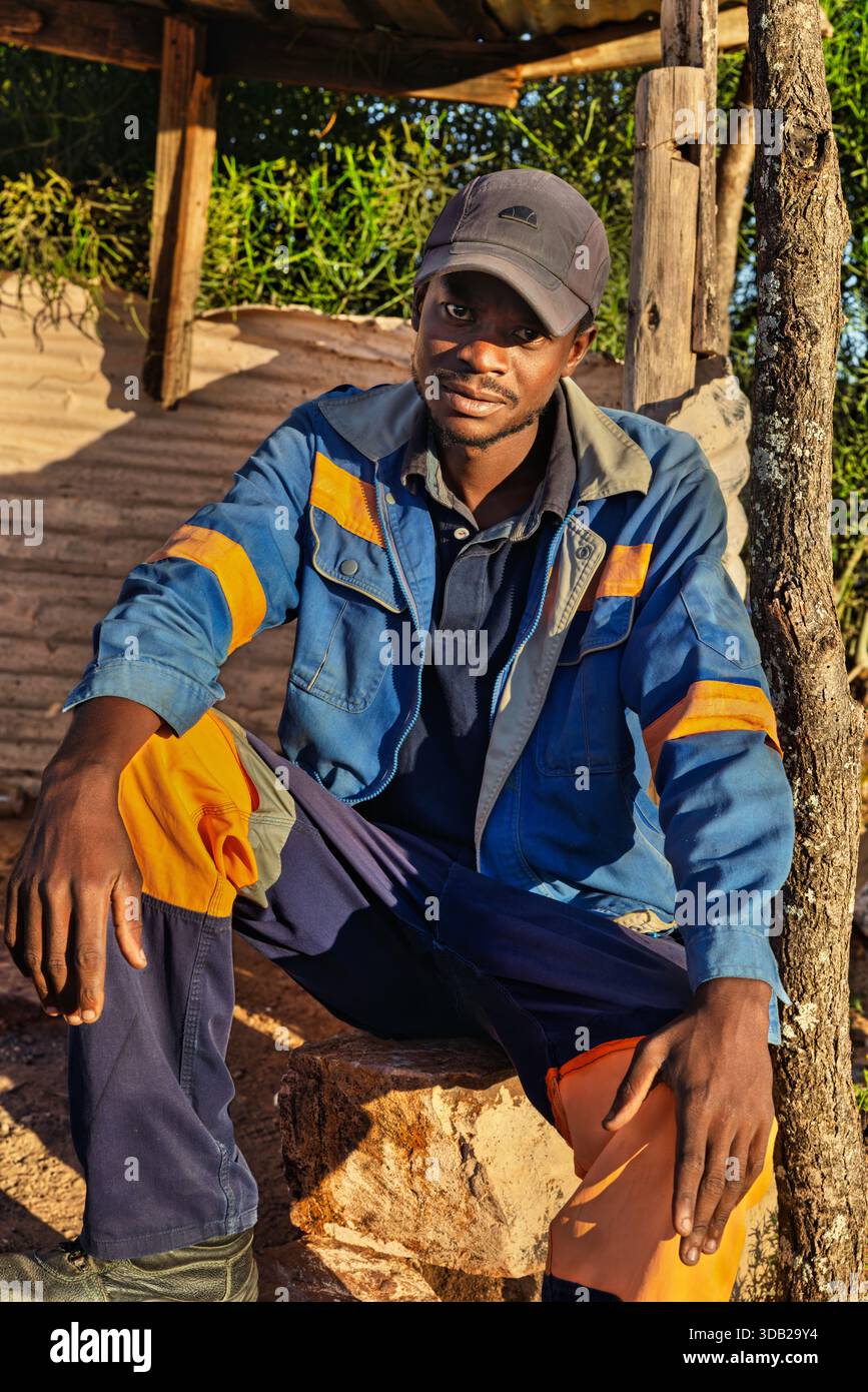 Einzelner afrikanischer Arbeiter sitzt draußen auf einer Steinbank bei Sonnenaufgang, Untergang hat gewellte Metall- und Holzstützen, Johannesburg, Südafrika, Stockfoto