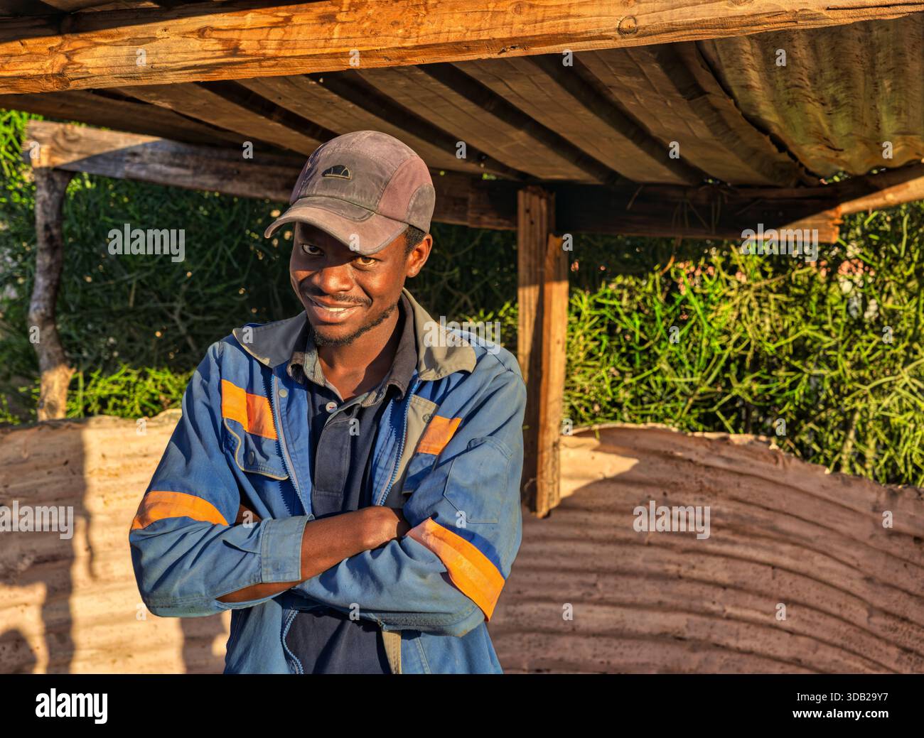 Einzelne afrikanische Männer arbeiten draußen bei Sonnenaufgang, Schuppen mit gewellten Metall- und Holzstützen, Johannesburg, Südafrika, blaue Arbeitskleidung Stockfoto