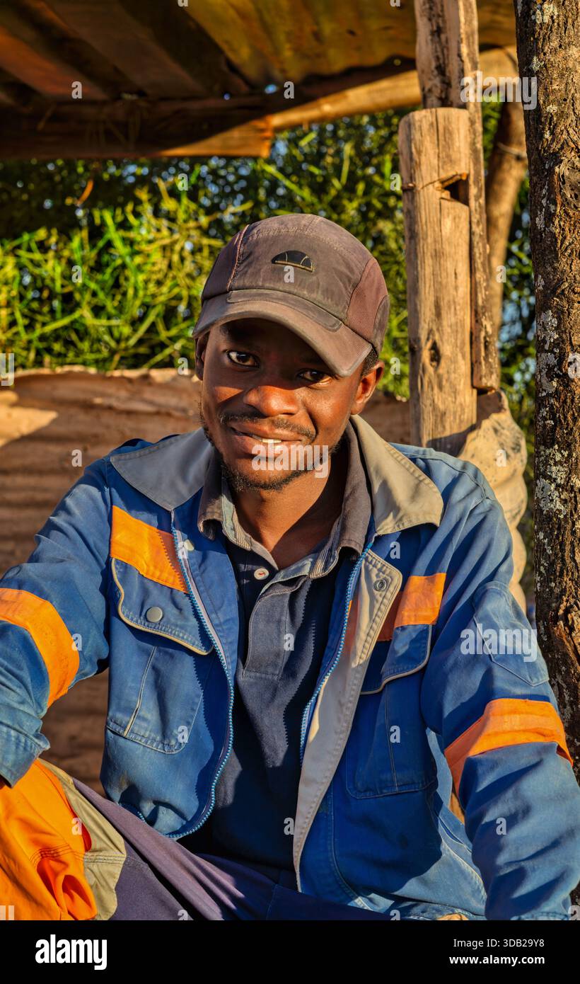 Einzelner afrikanischer Arbeiter sitzt draußen auf einer Steinbank bei Sonnenaufgang, Untergang hat gewellte Metall- und Holzstützen, Johannesburg, Südafrika, Stockfoto