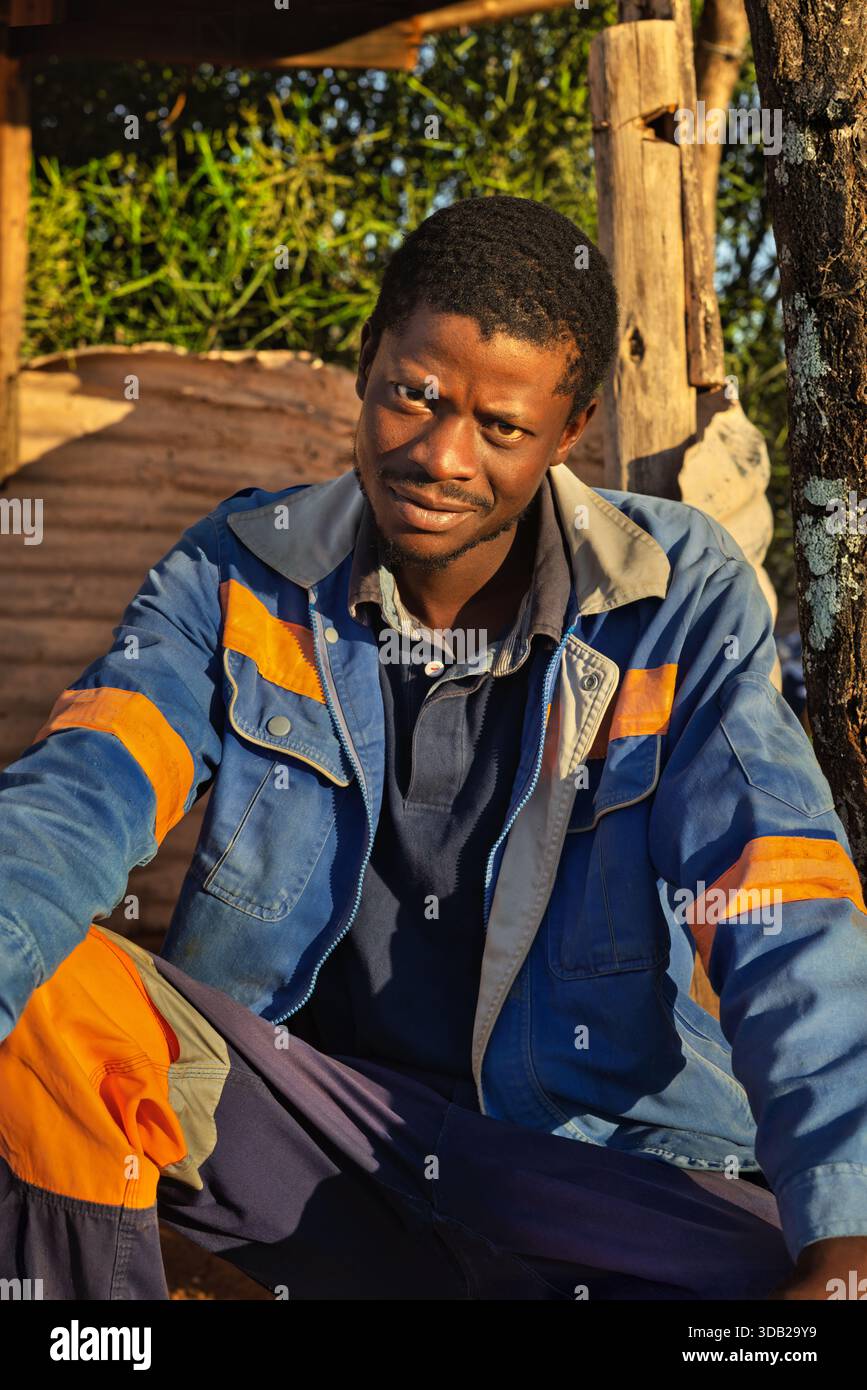 Einzelner afrikanischer Arbeiter sitzt draußen auf einer Steinbank bei Sonnenaufgang, Untergang hat gewellte Metall- und Holzstützen, Johannesburg, Südafrika, Stockfoto