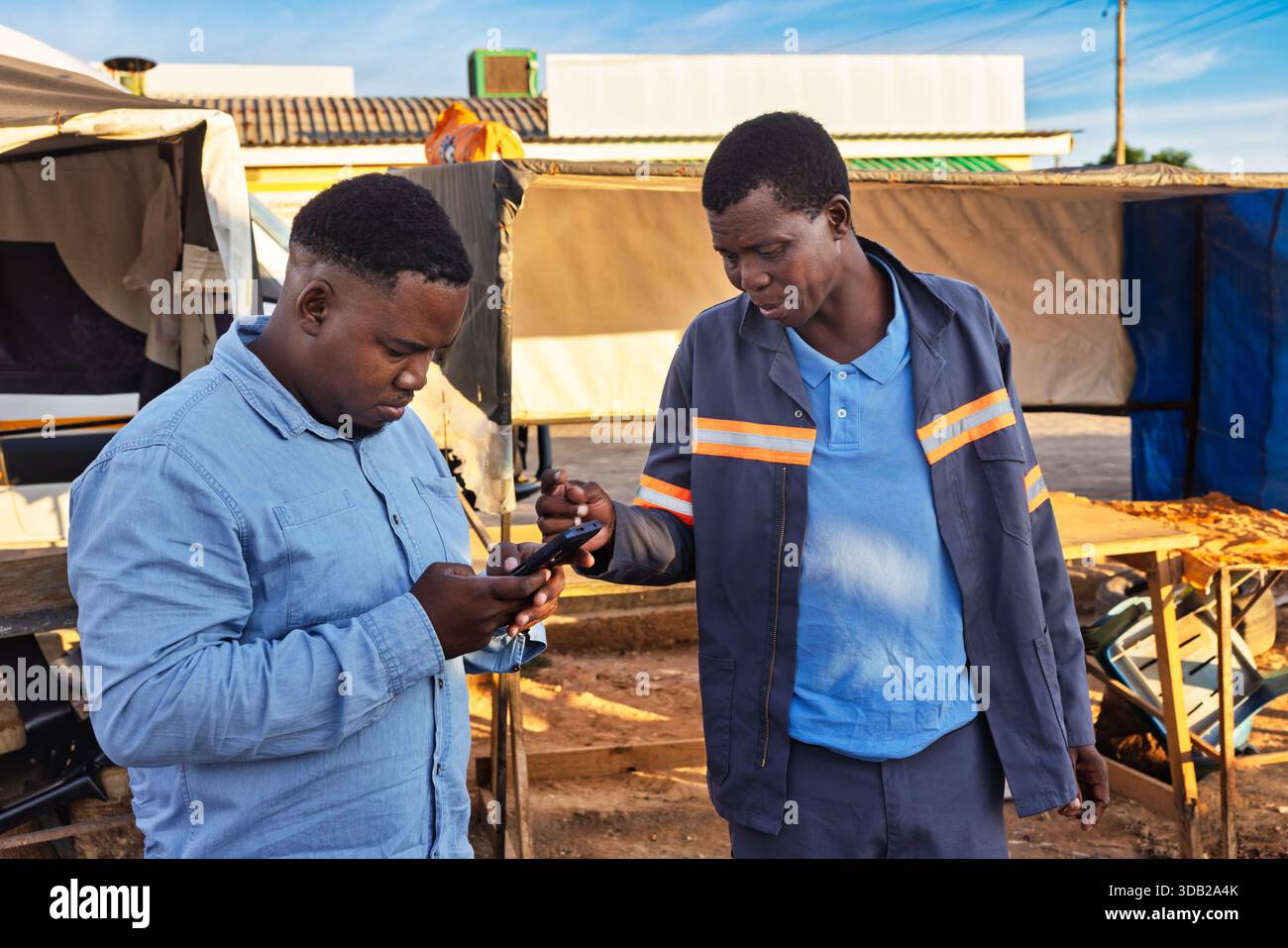 Zwei junge afrikanische Männer benutzen ein Telefon in der Altstadt am Bahnhofshandel bei Sonnenaufgang, Johannesburg, Südafrika, Freizeit- und Arbeitskleidung Stockfoto