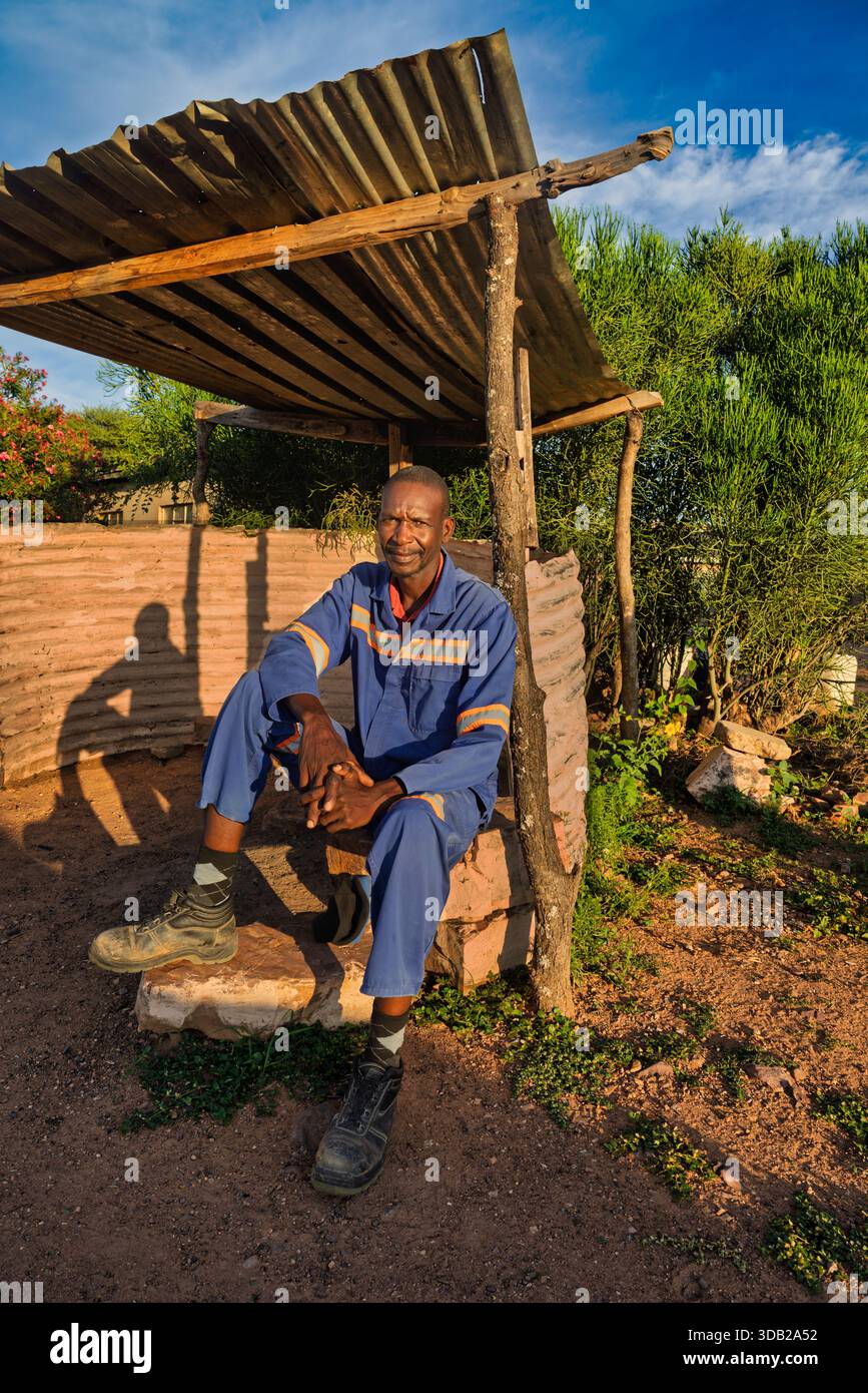 Einzelner afrikanischer Arbeiter sitzt draußen auf einer Steinbank bei Sonnenaufgang, Untergang hat gewellte Metall- und Holzstützen, Johannesburg, Südafrika, Stockfoto