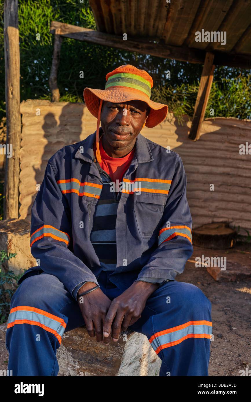 Einzelne afrikanische Männer sitzen draußen auf einer Steinbank bei Sonnenaufgang, Einstellung mit gewellten Metall- und Holzstützen, Johannesburg, Südafrika, blauer wo Stockfoto